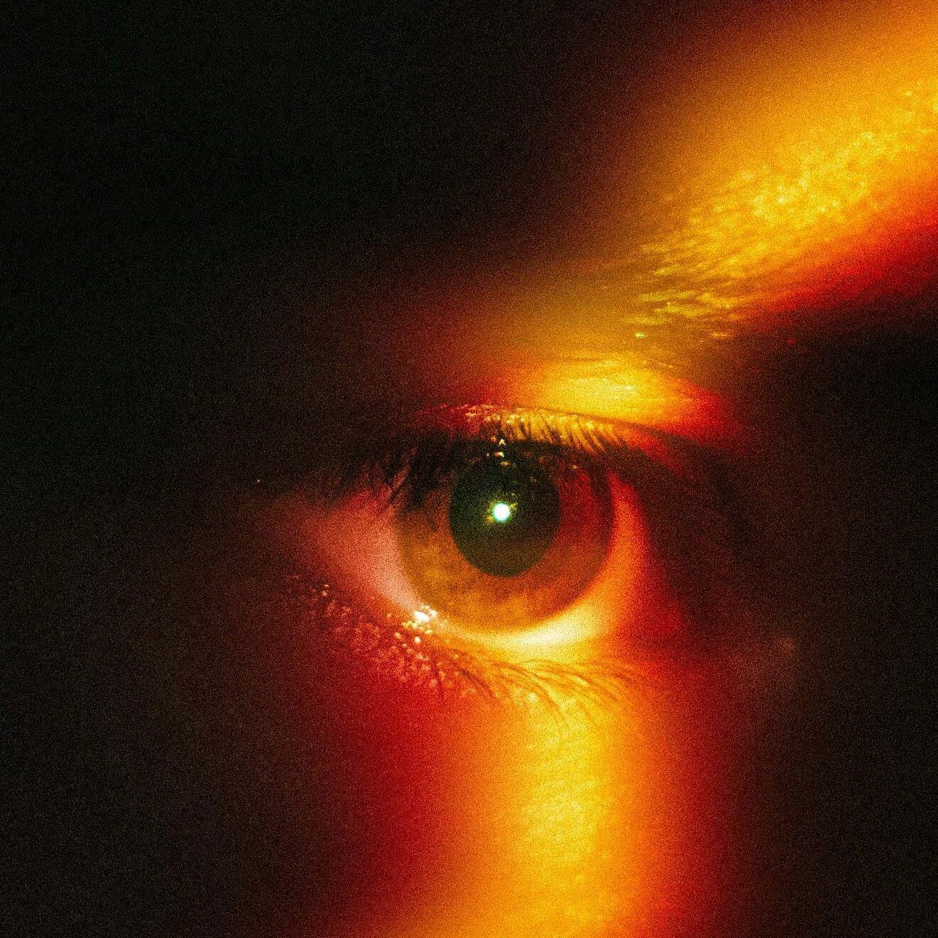 A captivating close-up of an eye with dramatic rainbow light effect in warm tones.