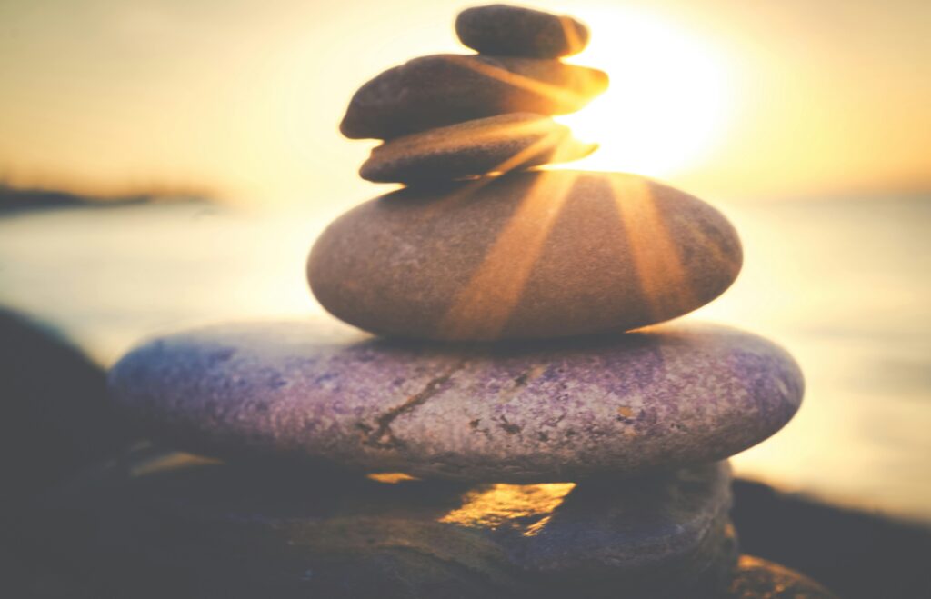 Stacked stones by the ocean create a tranquil scene during a beautiful sunset.